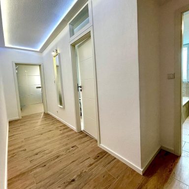 Heller Flur mit Holzparkett und modernen Türen, beleuchtet von einer Deckenleuchte.
