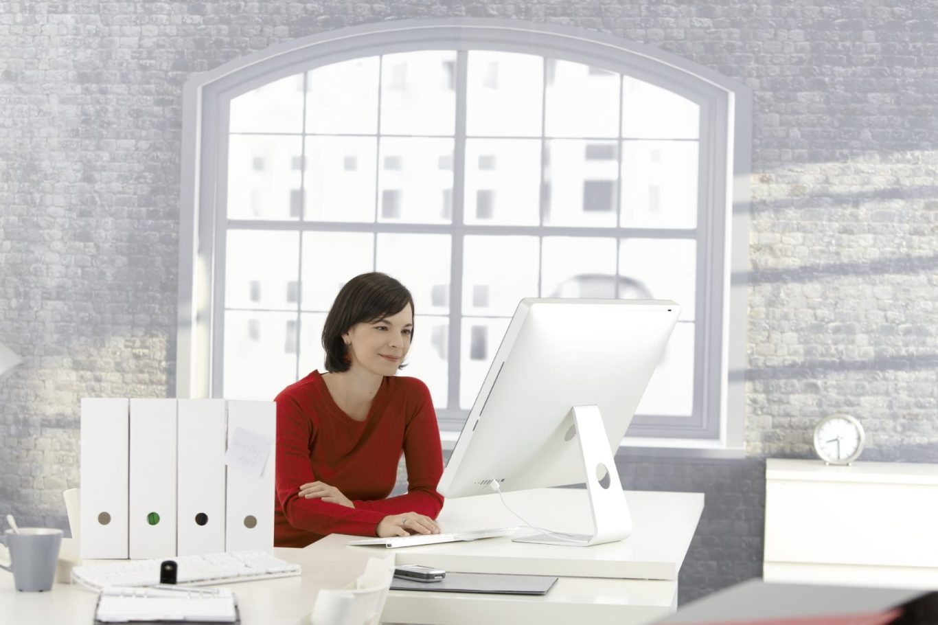 Frau in rotem Oberteil sitzt vor einem Computer in einem modernen Büro.