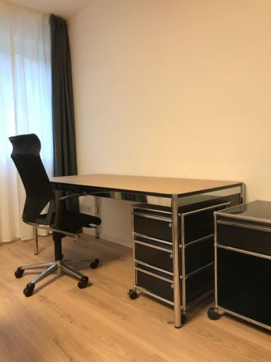 Schreibtisch mit schwarzem Bürostuhl und rollbarem Aktenschrank in einem hellen Raum.