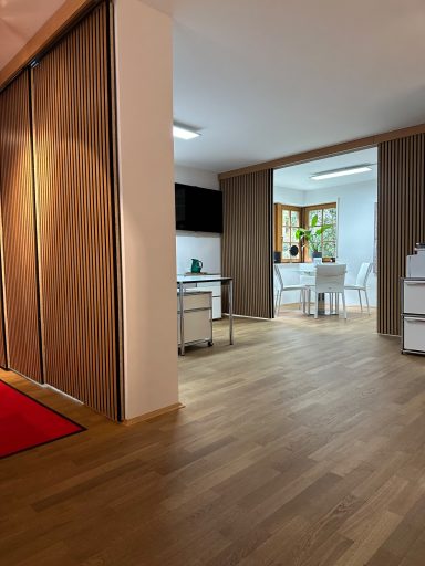 Moderner Raum mit Holzfußboden, hellem Mobiliar und Sicht auf angrenzenden Besprechungsbereich.