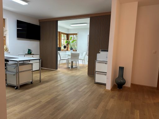 Modernes, helles Zimmer mit Holzfußboden, Schreibtisch und Zugang zum Essbereich.
