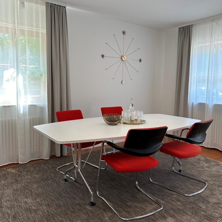 Moderne Essgruppe mit weißem Tisch und roten Stühlen, umgeben von hellem Vorhang.