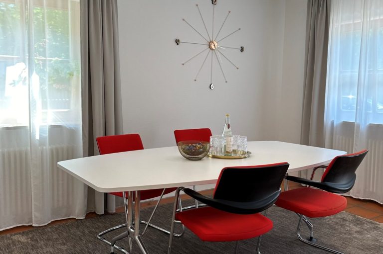 Moderne Essgruppe mit weißem Tisch und roten Stühlen in einem hellen Raum.
