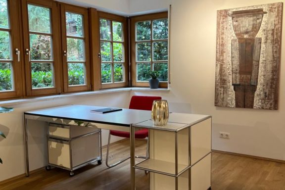 Helles Büro mit Schreibtisch, rotem Stuhl und Kunstwerk an der Wand.