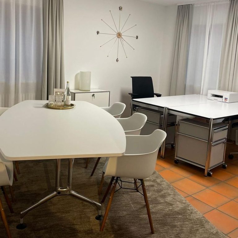 Ein Schreibtisch mit Laptop, Stuhl, Lampe und einem kleinen Pflanzenarrangement.