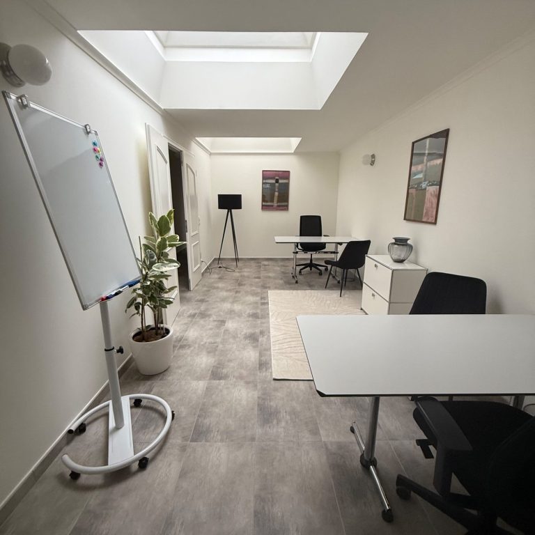 Büro Grünwald Arbeitsplatz 30qm Moderne Büroumgebung mit Laptop, Schreibgerät und Tischlampe. Pflanze im Hintergrund.