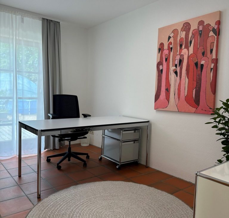 Ein moderner Schreibtisch mit Laptop, Stuhl, Lampe und einer Pflanze in einem hellen Raum.