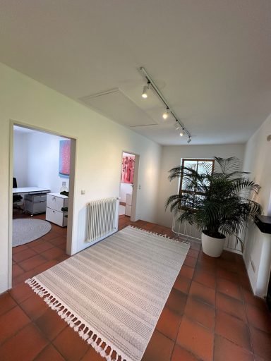 Heller Eingangsbereich mit Teppich, Pflanzen und Bürozimmer im Hintergrund.