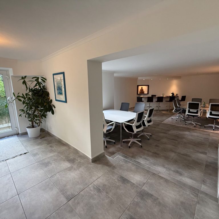 Moderne Büroumgebung mit Laptop, Schreibutensil, Pflanze und Lampen im Hintergrund.