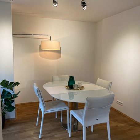 Heller Essbereich mit einem ovalen Tisch, vier weißen Stühlen und einer Pflanzenarrangement.
